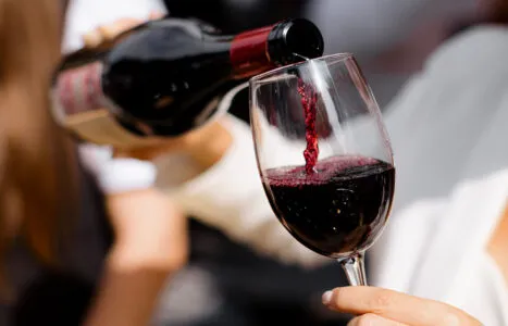 Close-up of a person pouring red wine into a glass at an outdoor event, showcasing wine's elegance
