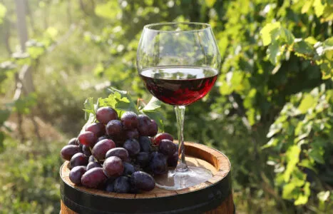 Tasty wine in glass and grapes on wooden barrel outdoors